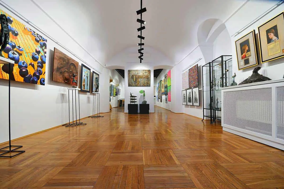 Długa sala galerii pod sklepieniem, z obrazami na ścianach i rzeźbami w gablotach