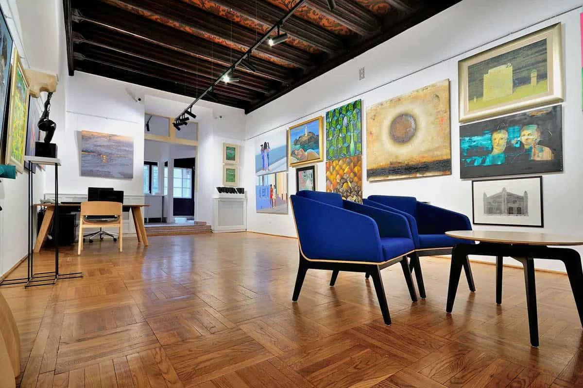 Sala wystawowa Kersten Gallery z drewnianym stropem, obrazami na ścianach i fotelami dla gości